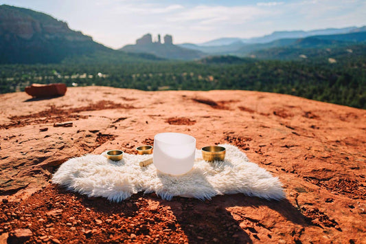 Harnessing Energy: A Guide to Connecting with Sedona's Spiritual Vortexes. This image shows sound healing bowls laid out on a fur on the red rocks with cathedral rock formation blurred in the background.