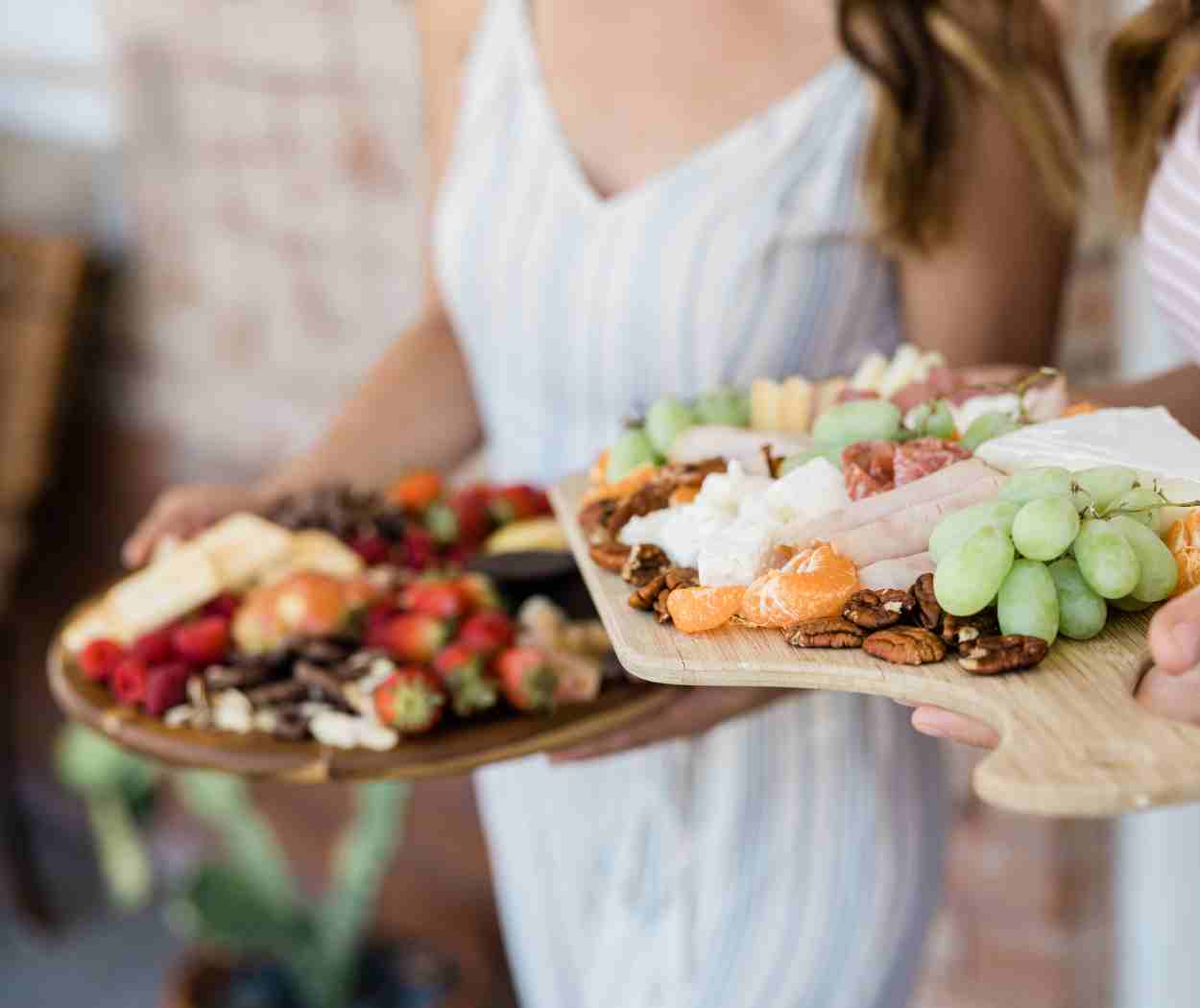 Two women carrying wooden boards with fresh fruit displayed. Vacation Delivery Service offers delivery of fresh fruits in Sedona.