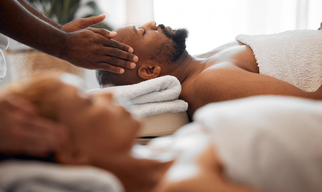 Discover the Healing Art of Tui-na Bodywork. A couple is are laying face up on massage tables. The man is in focus and a massage therapist has her hand on either side of his head.