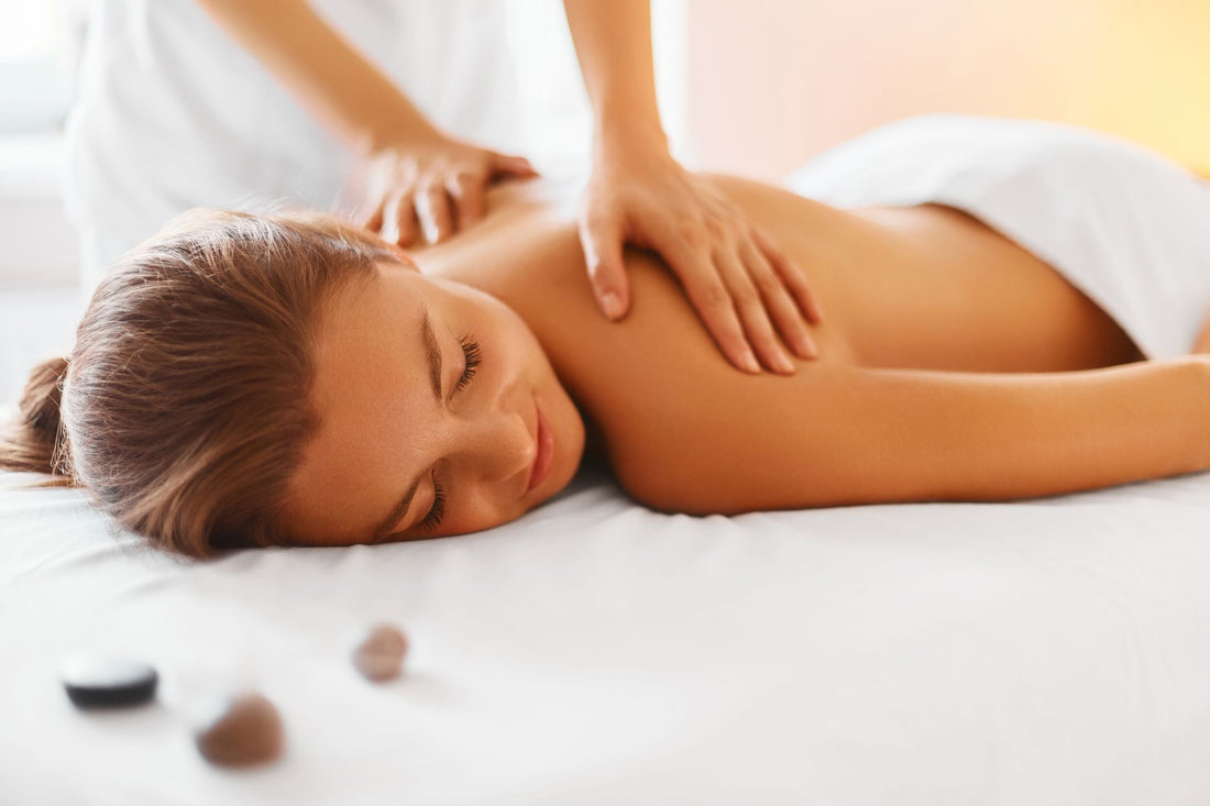 Unveiling the Therapeutic Marvels of Deep Tissue Massage. A young woman is laying face down on a massage table with the massage therapists has her hands on her back.